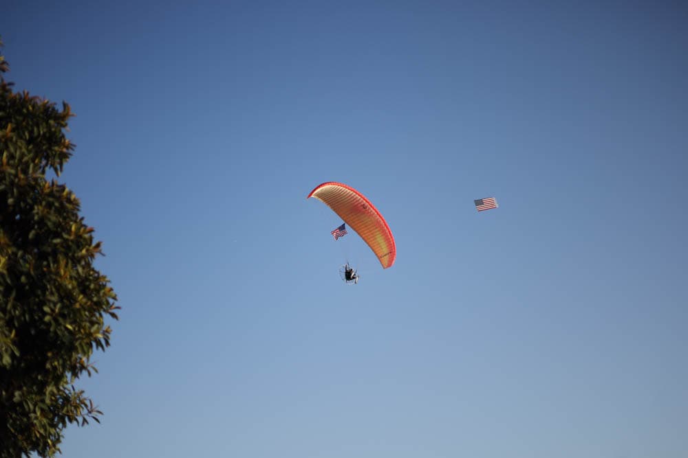 A paramotor pilot flies an American flag over the beach at dusk
