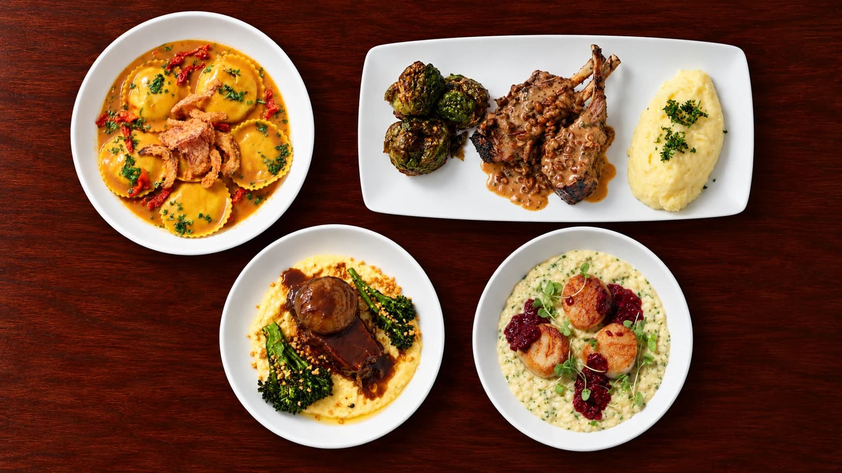 Top-down view of ravioli, lamb chops with Brussels sprouts and mashed potatoes, braised short rib on polenta, and scallops with risotto on a dark wood table.